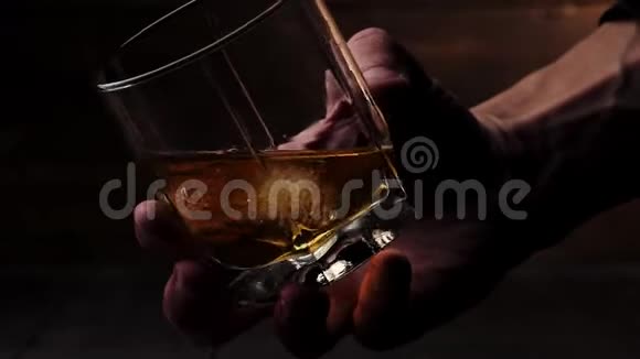 豪华威士忌人慢慢地在杯子里用冰块在木制背景下搅拌金色威士忌不倒翁威士忌波旁酒视频的预览图