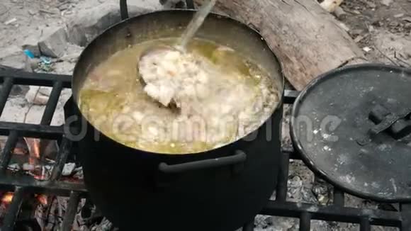 一只手拿着一个瓢把配料混合在沸腾的汤里在大自然的大锅里做饭徒步旅行者的食物营地游客视频的预览图