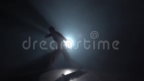 剪影男在黑暗中对着灯光聚光灯练习卡波伊拉慢动作视频的预览图