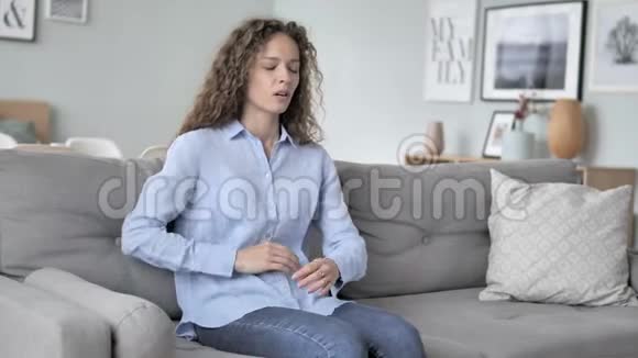 卷发妇女脊柱背疼坐在沙发上视频的预览图