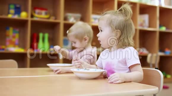 小孩子坐在桌子旁他们用勺子自己吃盘子里的东西然后有人视频的预览图