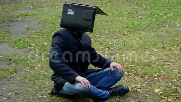 一个穿着外套的男人坐在空地上头上戴着笔记本电脑沉思着视频的预览图