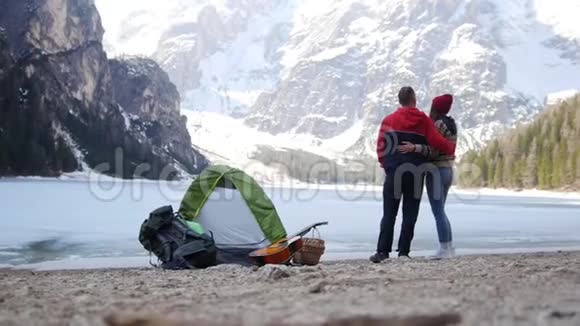 年轻夫妇站在冰冻的湖面上欣赏山景视频的预览图
