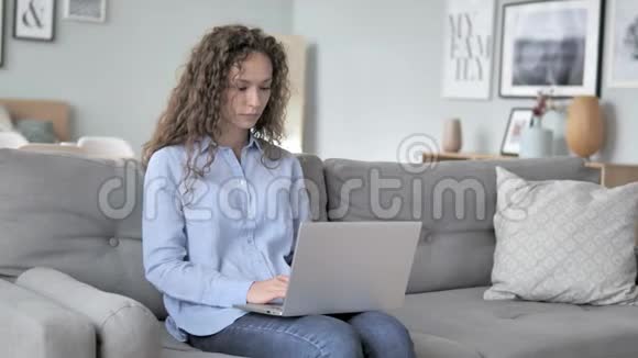 卷发女人头痛坐在沙发上用笔记本电脑工作视频的预览图