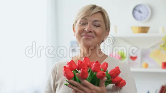 年长的金发女郎用相机嗅着郁金香花束节日礼物视频的预览图