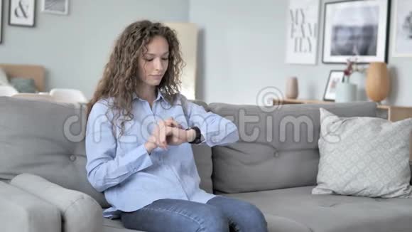 卷发女人坐在沙发上用智能手表视频的预览图