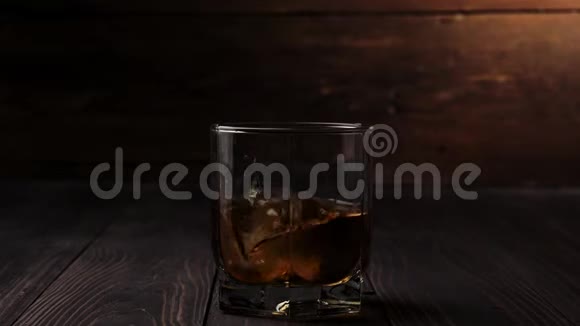豪华威士忌冰块落在一杯金色威士忌中放在木制桌子上背景是木制的不倒翁威士忌视频的预览图