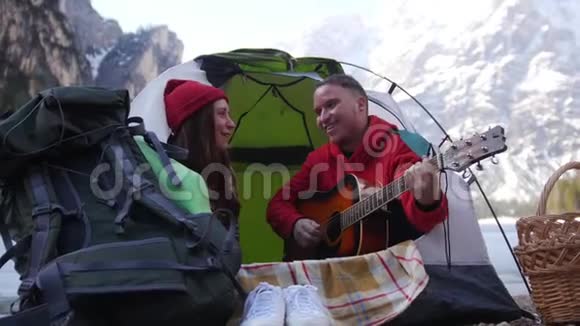 年轻夫妇在旅行坐在帐篷里用吉他唱歌视频的预览图