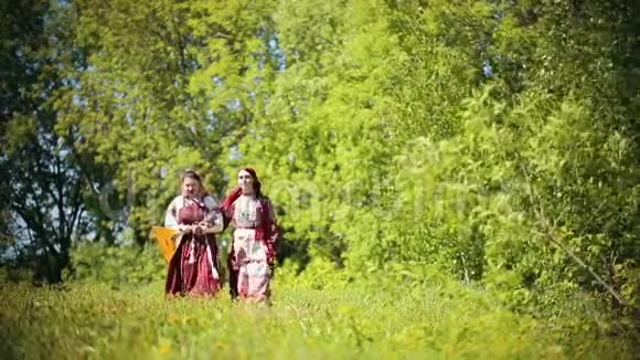 两个穿着俄罗斯传统服装的年轻女人走在田野上唱着一首歌其中一个拿着巴拉莱卡视频的预览图
