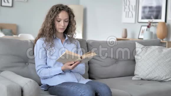 卷发女人坐在沙发上看书视频的预览图