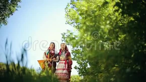 两个穿着俄罗斯传统服装的年轻女子走在田野上唱着一首歌其中一个拿着巴拉莱卡视频的预览图