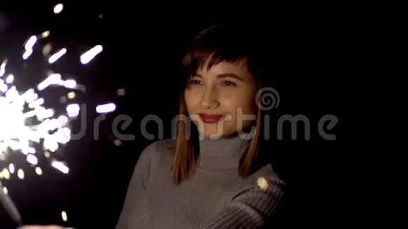 女孩脸上带着微笑手里拿着火花庆祝圣诞节享受着灯光的美丽视频的预览图