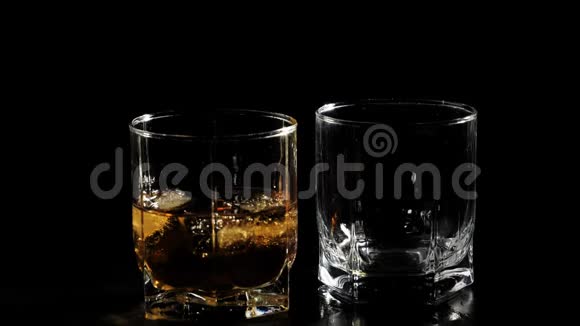 豪华威士忌手把金色的威士忌从一个方形的瓶子里倒入一个玻璃杯放在靠近玻璃杯的黑桌上里面有威士忌和冰视频的预览图