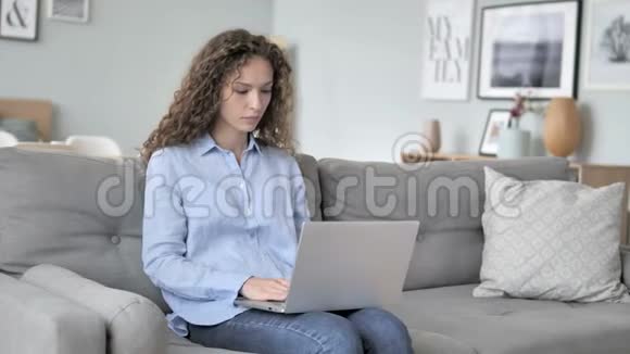 令人震惊的卷发女人在笔记本电脑上工作坐在沙发上视频的预览图