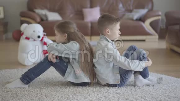 双胞胎男孩和女孩坐在客厅的地板上背对着对方生气兄妹关系视频的预览图