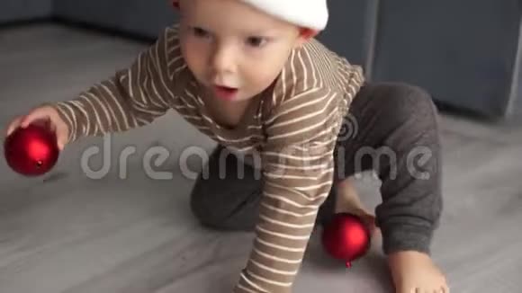 戴着圣诞老人羊毛帽的幼儿正在玩一个红色的圣诞球圣诞快乐新年快乐视频的预览图