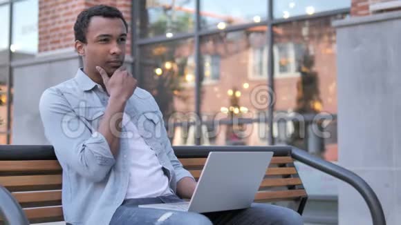 穿着笔记本电脑的非洲男人坐在长凳上视频的预览图