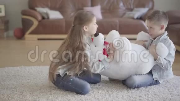 双胞胎男孩和女孩坐在地板上的客厅里不知道如何在他们之间分享一只大蝌蚪儿童视频的预览图