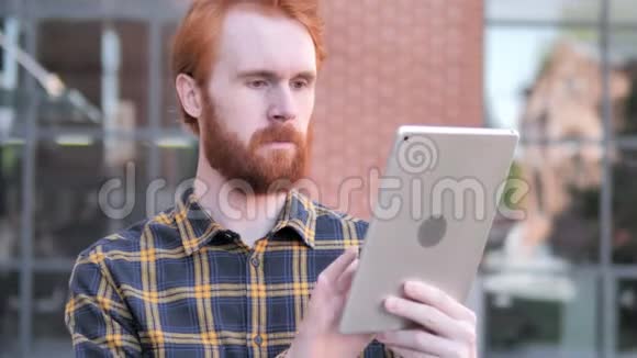 红发胡子年轻人在平板电脑上的户外视频聊天视频的预览图