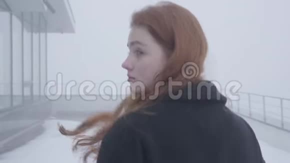年轻的红发美女一个人看有时在雾蒙蒙的雪天在餐馆附近转过身视频的预览图