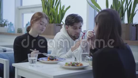三个朋友坐在餐厅里在舒适的地方吃午餐一边聊天一边微笑视频的预览图