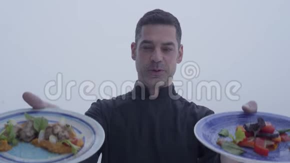 一位满脸笑容的留着胡子的厨师身着黑色制服端着两盘美味的菜肴站在视频的预览图