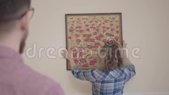 丈夫告诉妻子如何正确地根据水平把照片挂在墙上年轻的家庭搬到了视频的预览图