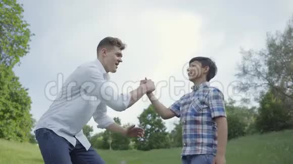 年轻的父亲和男孩击掌在户外握手爸爸和一个孩子在公园里玩得很开心友好家庭视频的预览图