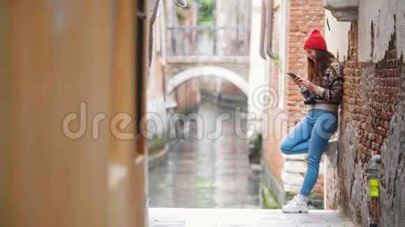 一个年轻的笑女站在威尼斯的街道上看着她的电话视频的预览图