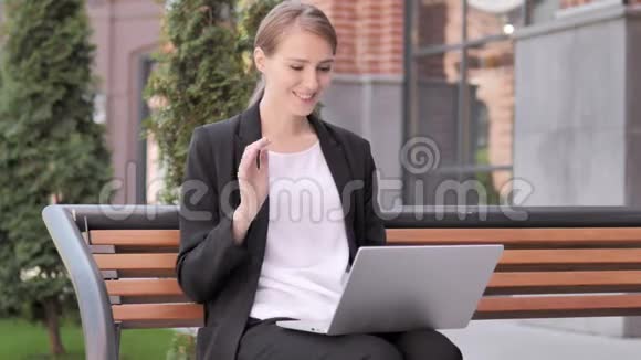 年轻女商人坐在长凳上在线视频聊天视频的预览图