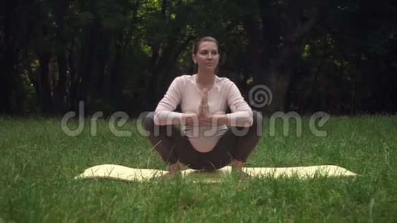 一位孕妇在公园里的地毯上练习瑜伽做体式马拉萨纳乌鸦的姿势或青蛙的姿势视频的预览图