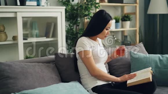 亚洲年轻的女士正在看书拿着一杯茶然后翻页坐在漂亮的沙发上喝酒视频的预览图