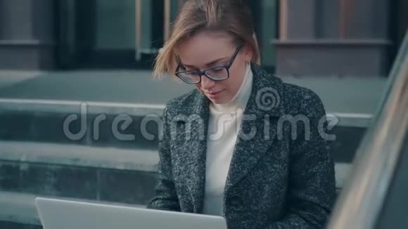 在户外工作的年轻女人穿外套的女孩坐在台阶上视频的预览图