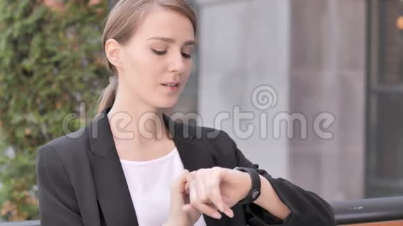 年轻的女商人用智能手表坐在户外视频的预览图