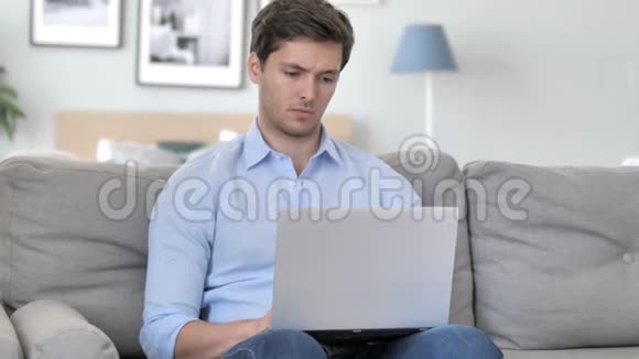 有头痛的帅哥坐在沙发上用笔记本电脑工作视频的预览图