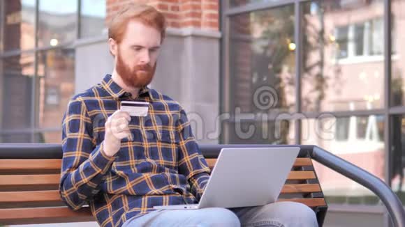 坐在长凳上的红胡子青年网上购物视频的预览图