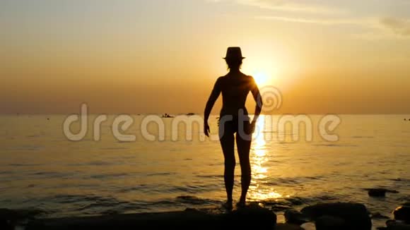 日落时海滩上一位年轻女子的剪影她穿着泳衣举起双手视频的预览图