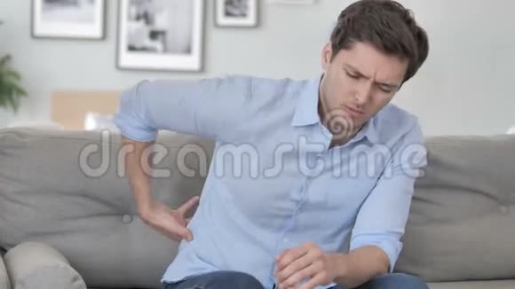 英俊的年轻人背脊疼痛坐在沙发上视频的预览图
