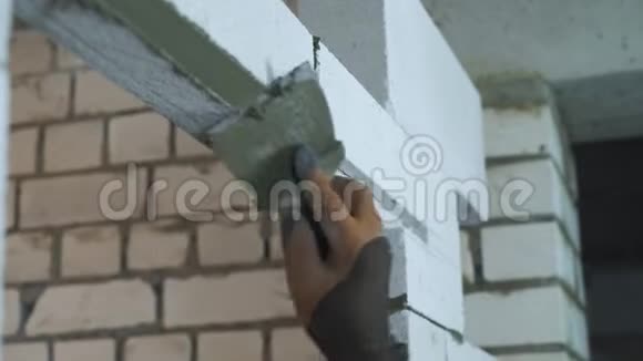 建筑工人手在手套上的视图在门口的积木上放置粘合剂混合物视频的预览图