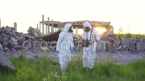两名穿着白色工作服和防护面罩的科学家在日落时测量辐射的肖像视频的预览图