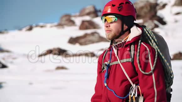 白种人的年轻登山者长着胡子站在雪坡上环顾四周遮住眼睛视频的预览图