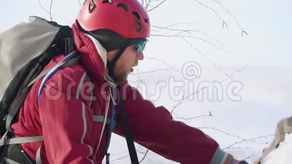 长胡子的登山者打破冰斧密集的雪以确保设备安全他穿得很暖和上面有一个背包和设备视频的预览图