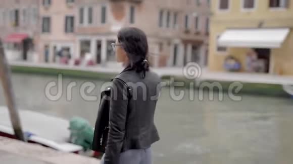 一个穿皮夹克的漂亮女孩在意大利威尼斯散步女游客对她在欧洲度假感到高兴视频的预览图