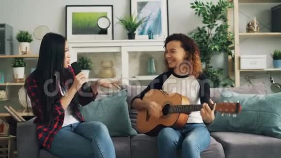 女朋友在家玩弹吉他在电视遥控器唱歌享受休闲活动视频的预览图
