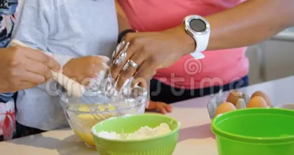 父亲和儿子把面粉倒入碗里母亲把鸡蛋搅拌4k视频的预览图