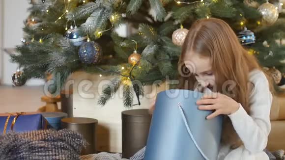 可爱的金发女孩打开了深蓝色的礼物盒她坐在圣诞树旁快乐的童年和圣诞节视频的预览图
