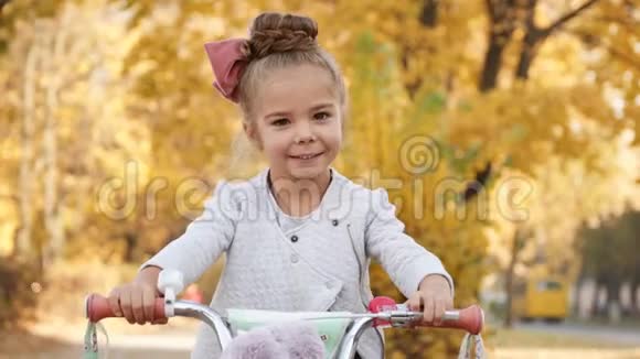 小女孩骑自行车在秋天的城市大道上视频的预览图