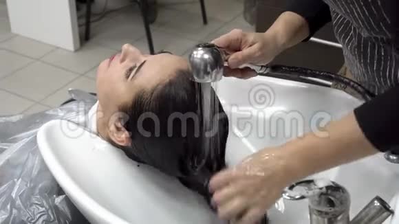 理发师在一家理发店里用一个白色的脸盆洗了一个美丽的东方女孩的头头发护理关门视频的预览图