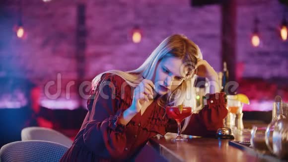 一位漂亮的无聊的年轻女子坐在酒保的旁边站着用一根稻草搅动饮料视频的预览图