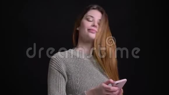 年轻美丽的白种人女孩的特写照片她用手机甩头发然后看着相机微笑着视频的预览图